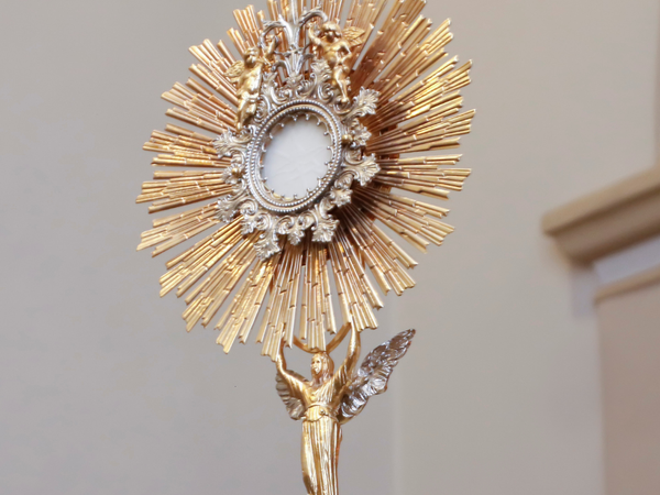 Golden monstrance with sunburst rays and angel figure for Catholic faith growth