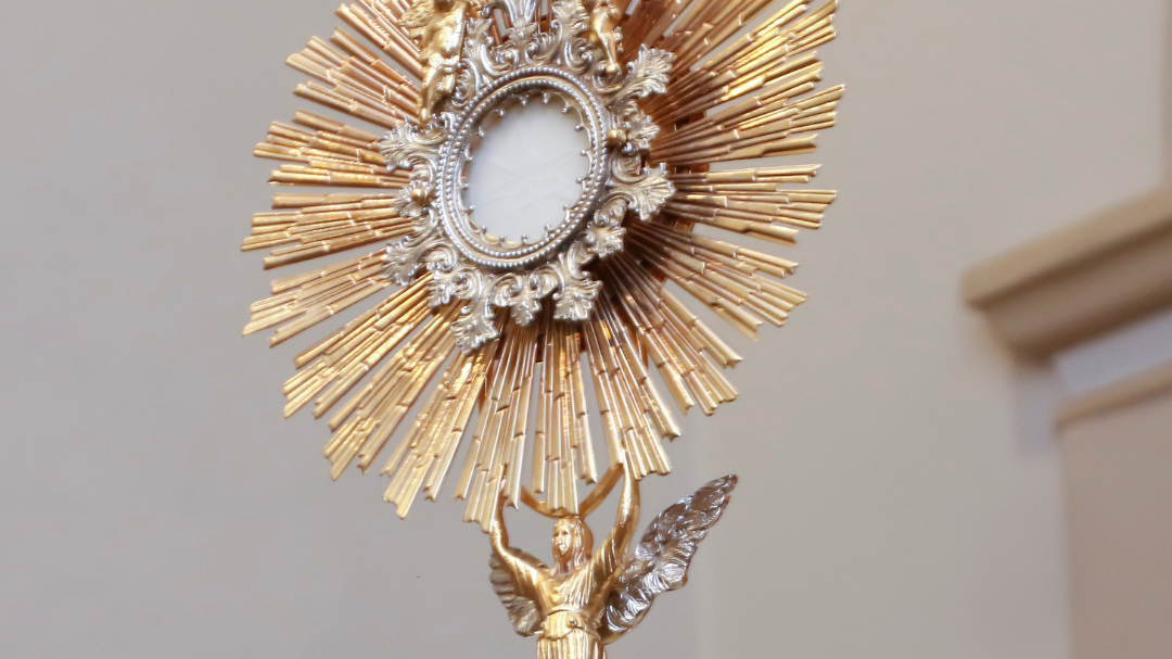 Golden monstrance with sunburst rays and angel figure for Catholic faith growth