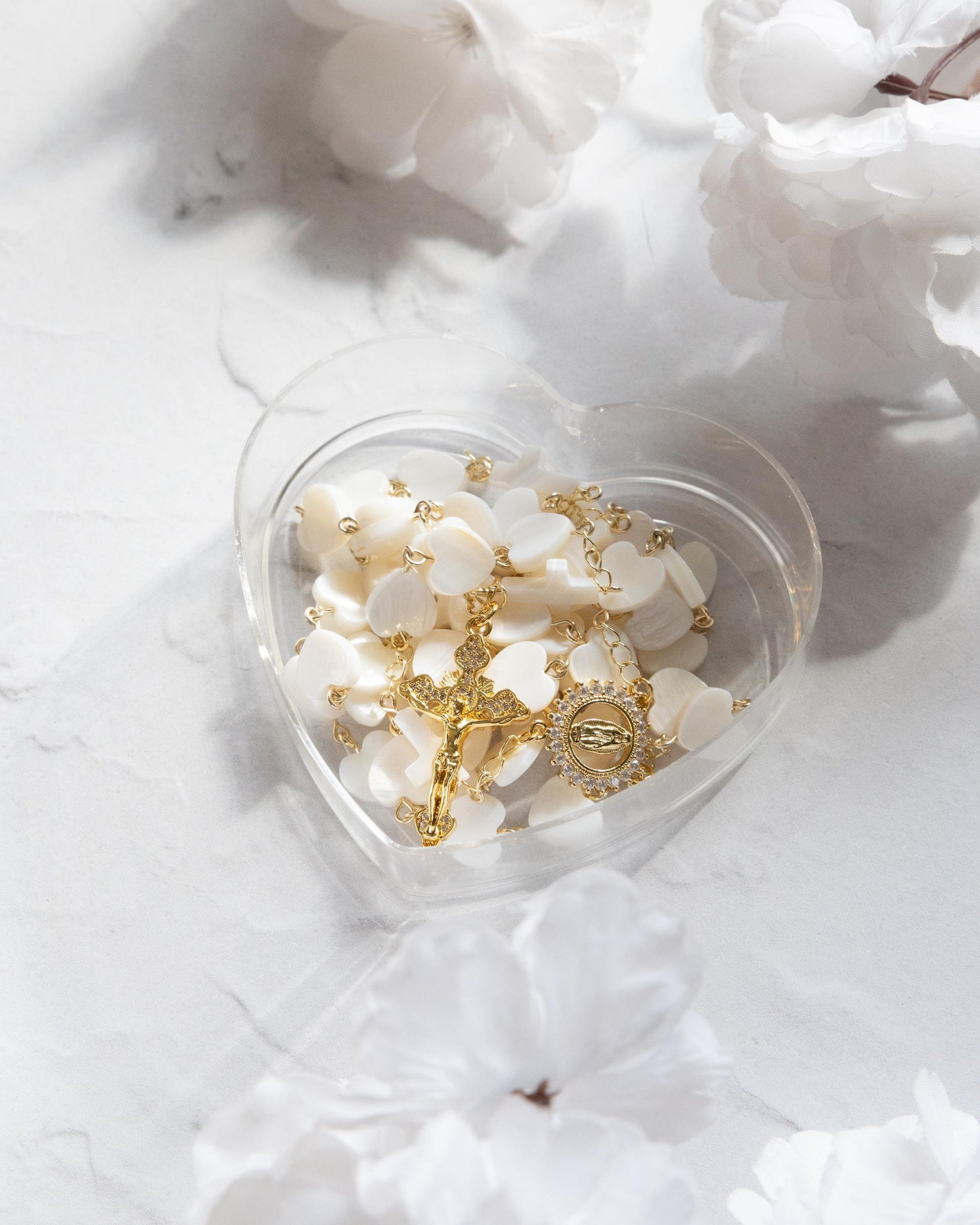 pearl heart shaped rosary displayed in a heart-shaped case surrounded by white flowers.