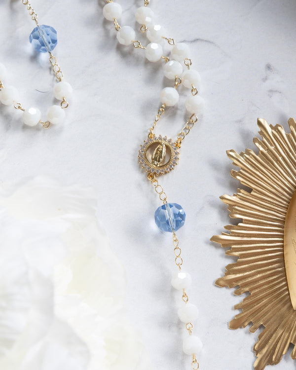 Elegant white beaded necklace with gold accents and a blue crystal centerpiece.