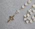 Close-up of a pearl heart shaped rosary with a gold crucifix and cross accents on a textured background.