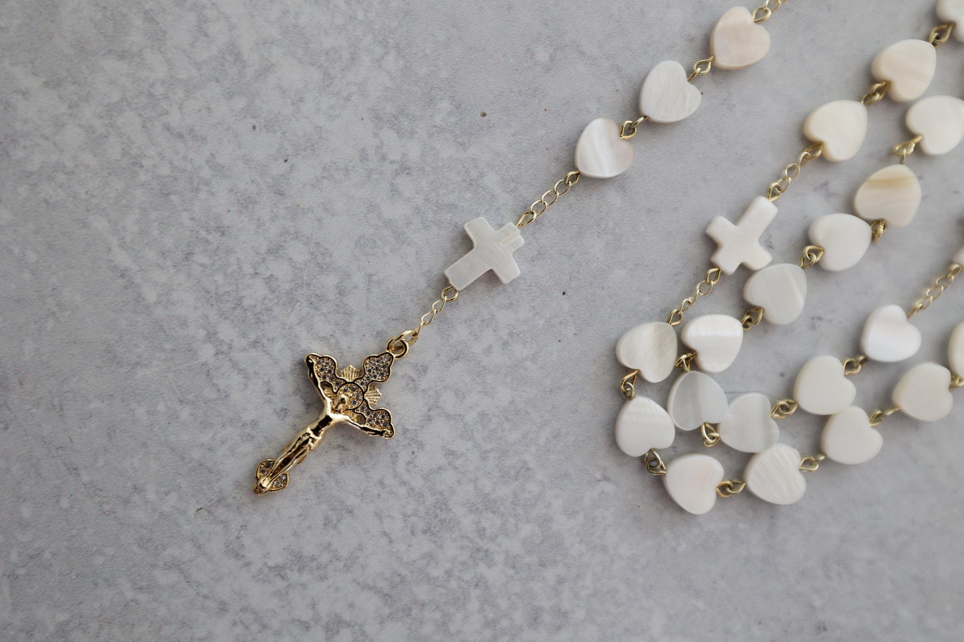 Close-up of a pearl heart shaped rosary with a gold crucifix and cross accents on a textured background.