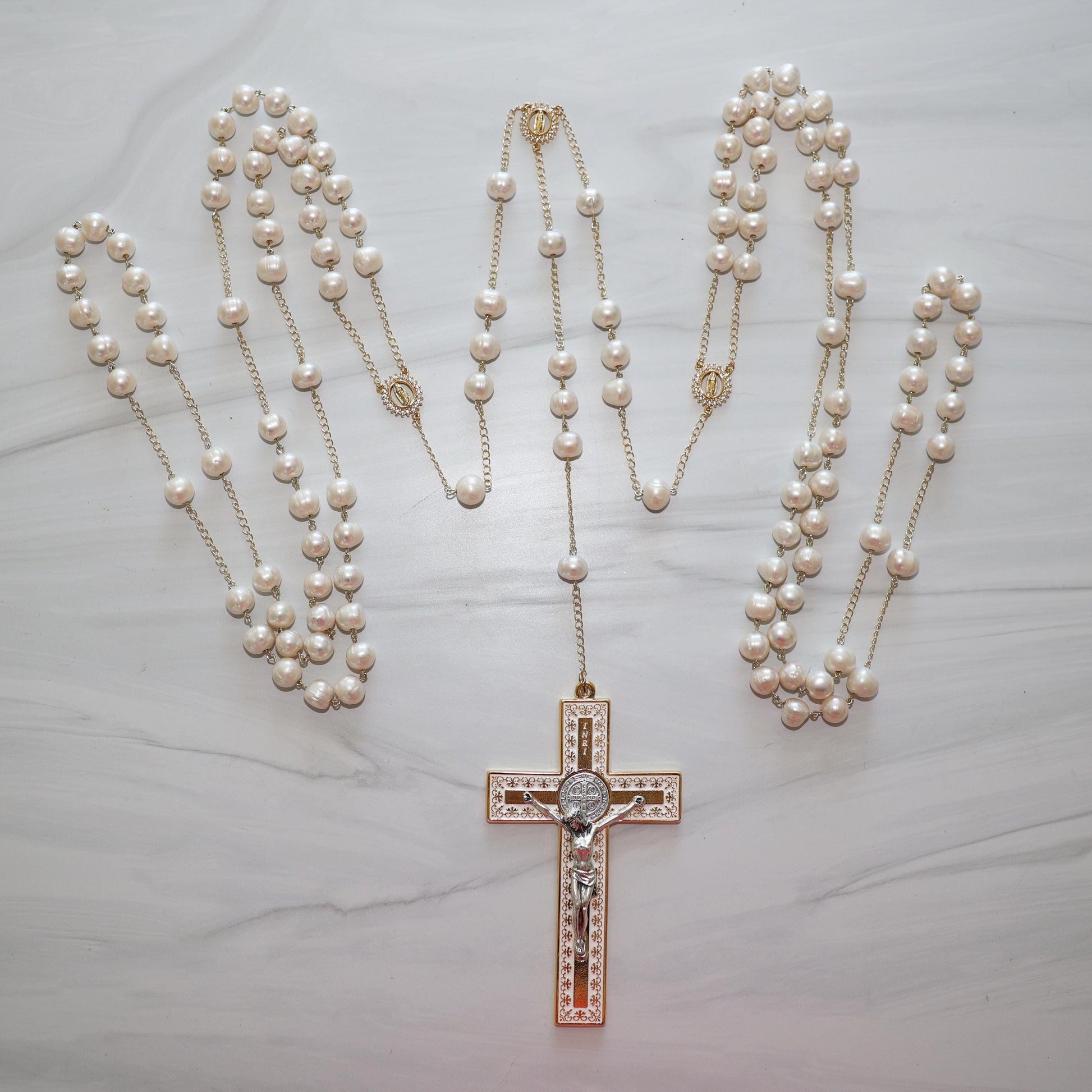 Freshwater pearl wedding lasso rosary with gold findings and a decorative cross pendant on a marble surface.