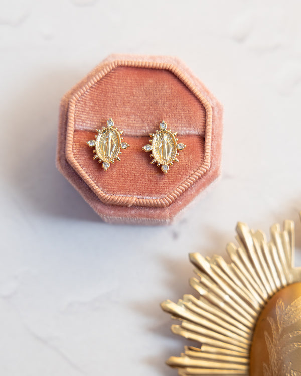 Gold-toned oval stud earrings featuring a detailed religious figure design surrounded by sparkling clear stones.