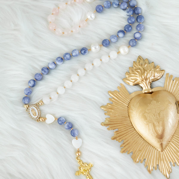A delicate blue and white beaded rosary with gold accents, featuring a heart-shaped centerpiece and a small cross pendant.