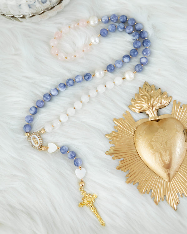A delicate blue and white beaded rosary with gold accents, featuring a heart-shaped centerpiece and a small cross pendant.