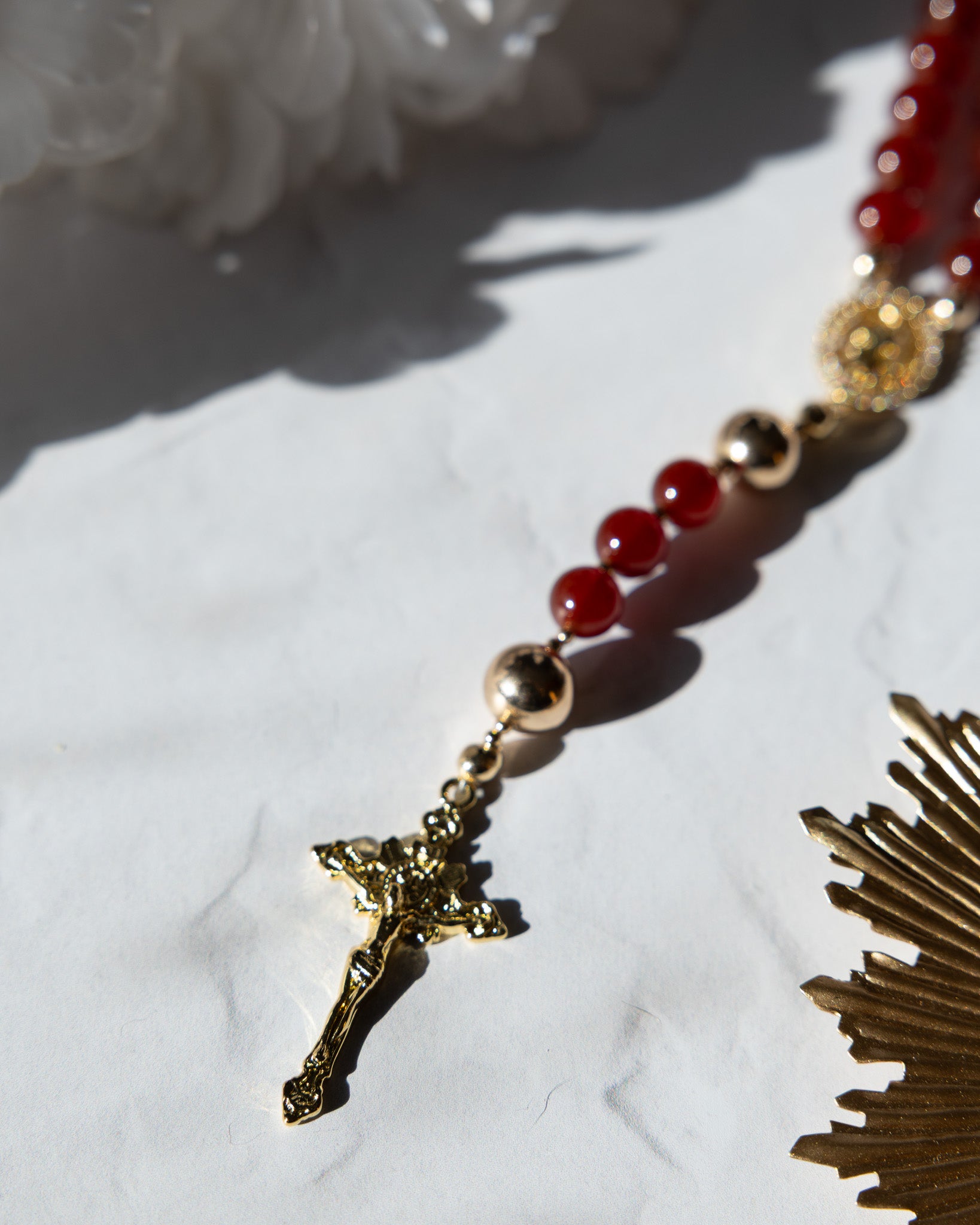 Gold-toned rosary with red agate beads and a detailed crucifix pendant.