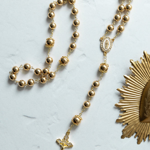 Gold-toned rosary with spherical beads, a detailed crucifix pendant, and an ornate medallion featuring the virgin mary.