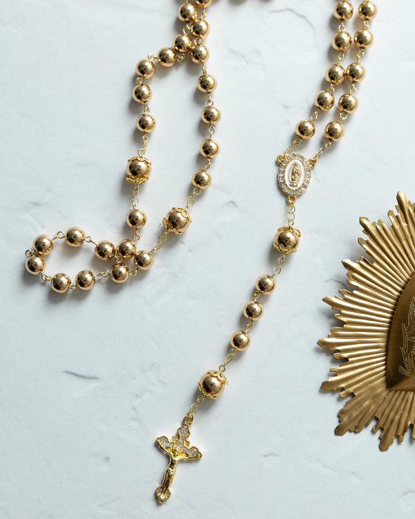 Gold-toned rosary with spherical beads, a detailed crucifix pendant, and an ornate medallion featuring the virgin mary.