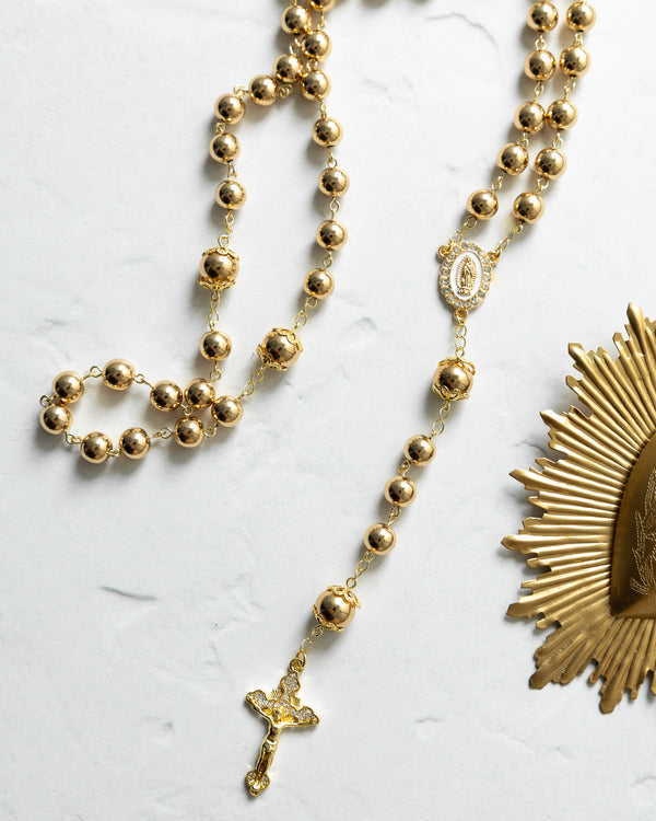 Gold-toned rosary with spherical beads, a detailed crucifix pendant, and an ornate medallion featuring the virgin mary.