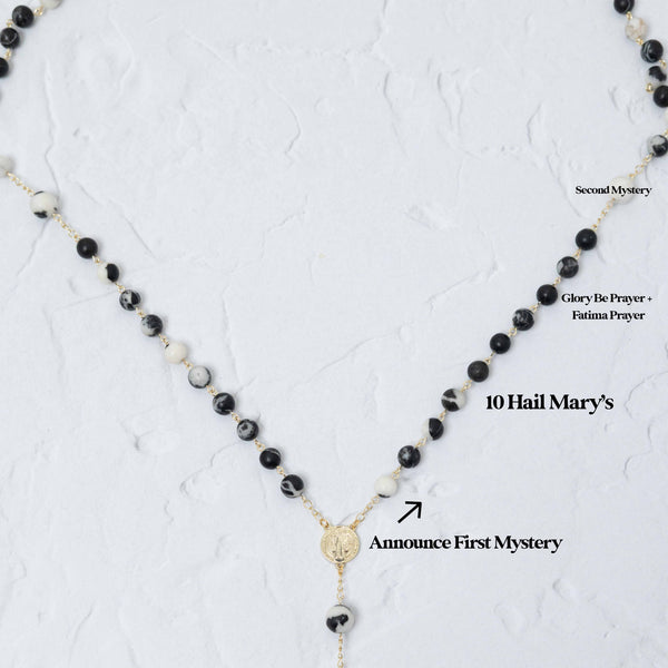 Black and white marbled stone beads strung on gold-toned metal with a central golden medallion.