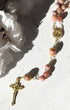A delicate pink rose quartz rosary with gold-toned metal accents and a detailed crucifix.