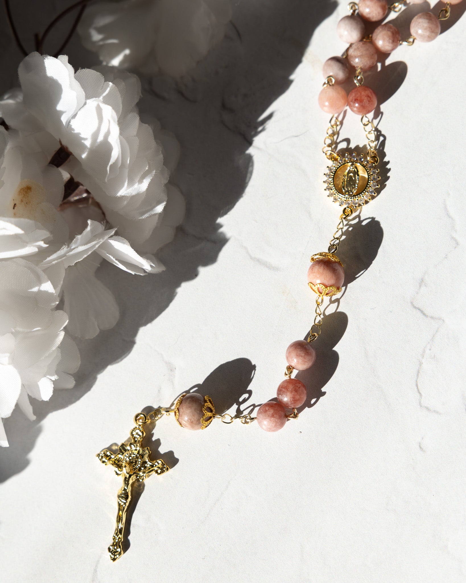 A delicate pink rose quartz rosary with gold-toned metal accents and a detailed crucifix.