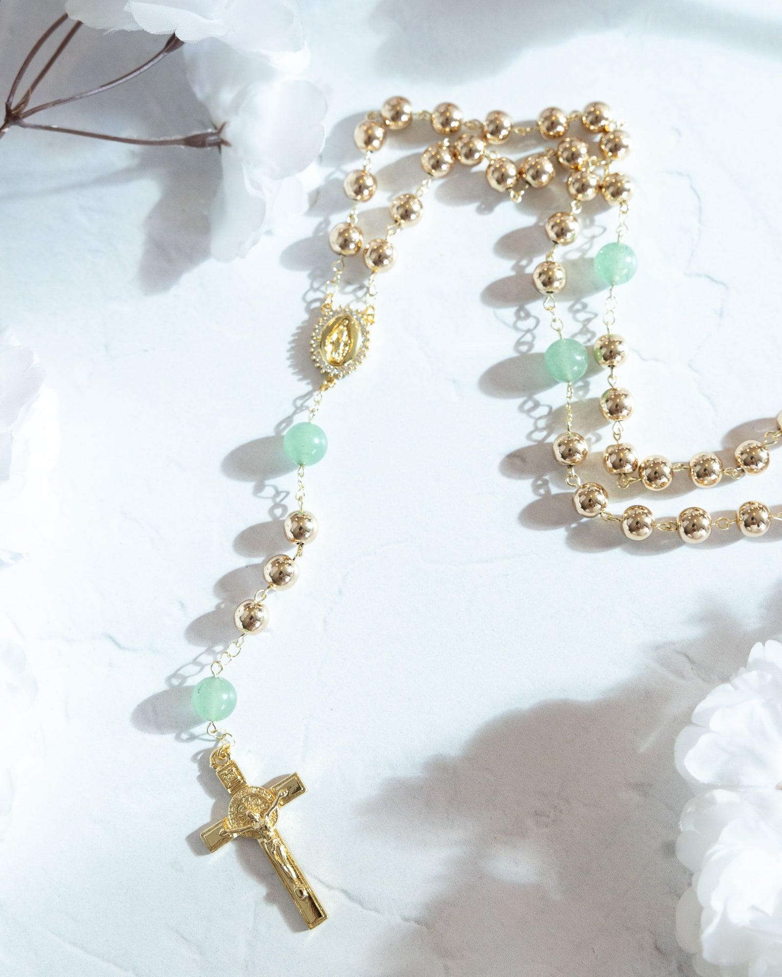 Gold-toned rosary with alternating spherical beads and translucent green jade-like stones, featuring an ornate central medallion and a detailed crucifix at the end.