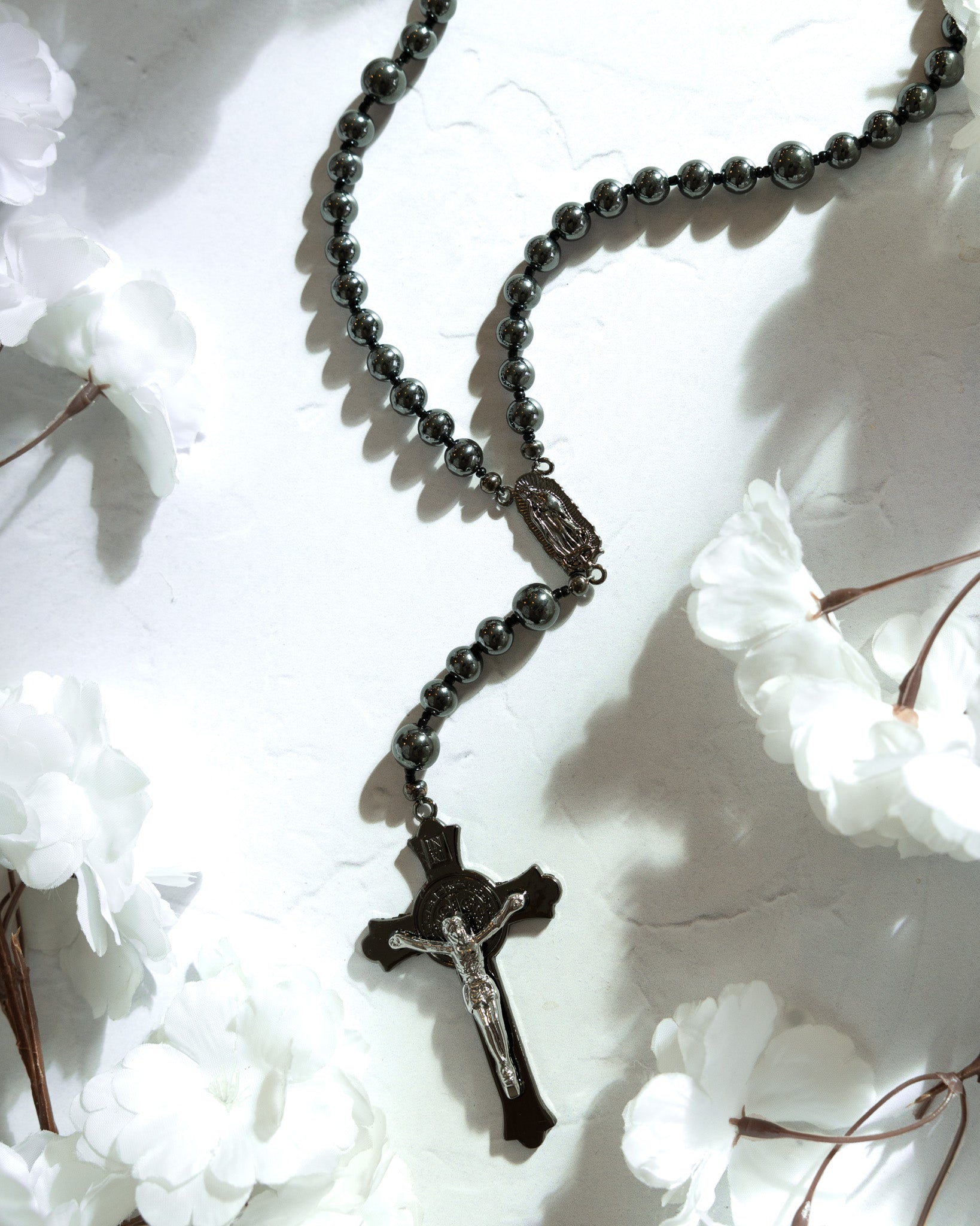 Black rosary with crucifix on a white floral background