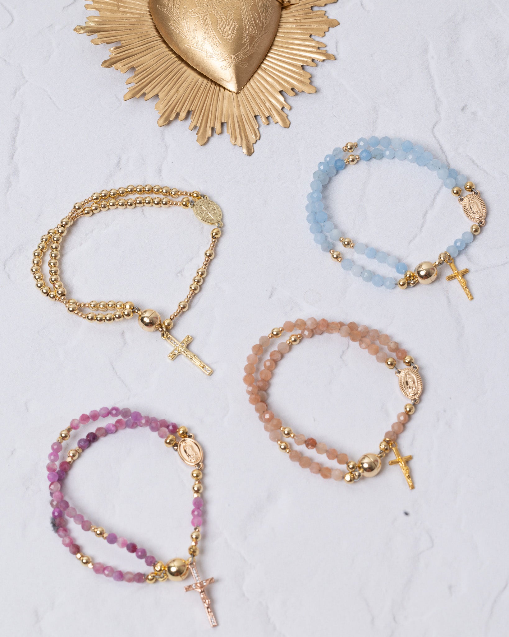 Set of four beaded rosary-style bracelets in pastel blue, pink, and peach tones with gold-toned metal accents and small crosses.