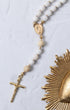 White beaded rosary with gold-toned metal accents and a crucifix.