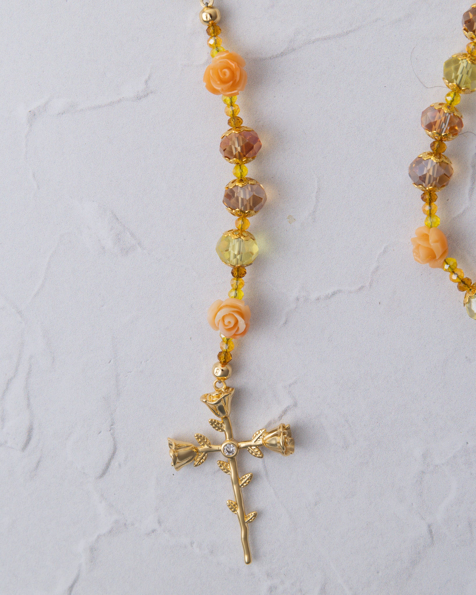 Metamorphosis rosary with delicate gold-toned chain, peach rose beads, amber crystals, and leafy cross pendant with gemstone