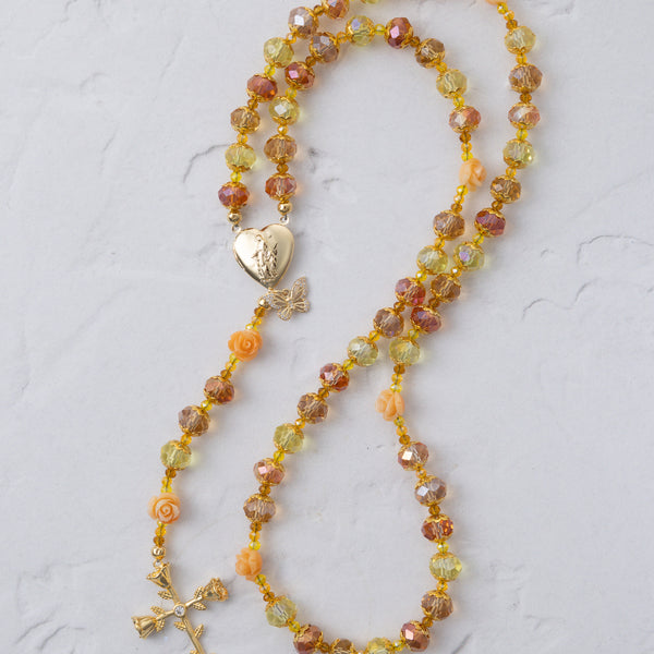 A delicate metamorphosis rosary with faceted amber yellow peach beads and gold heart locket with butterfly charm