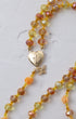 A delicate gold-toned metamorphosis rosary with faceted amber yellow beads and a heart-shaped locket pendant with butterfly charm