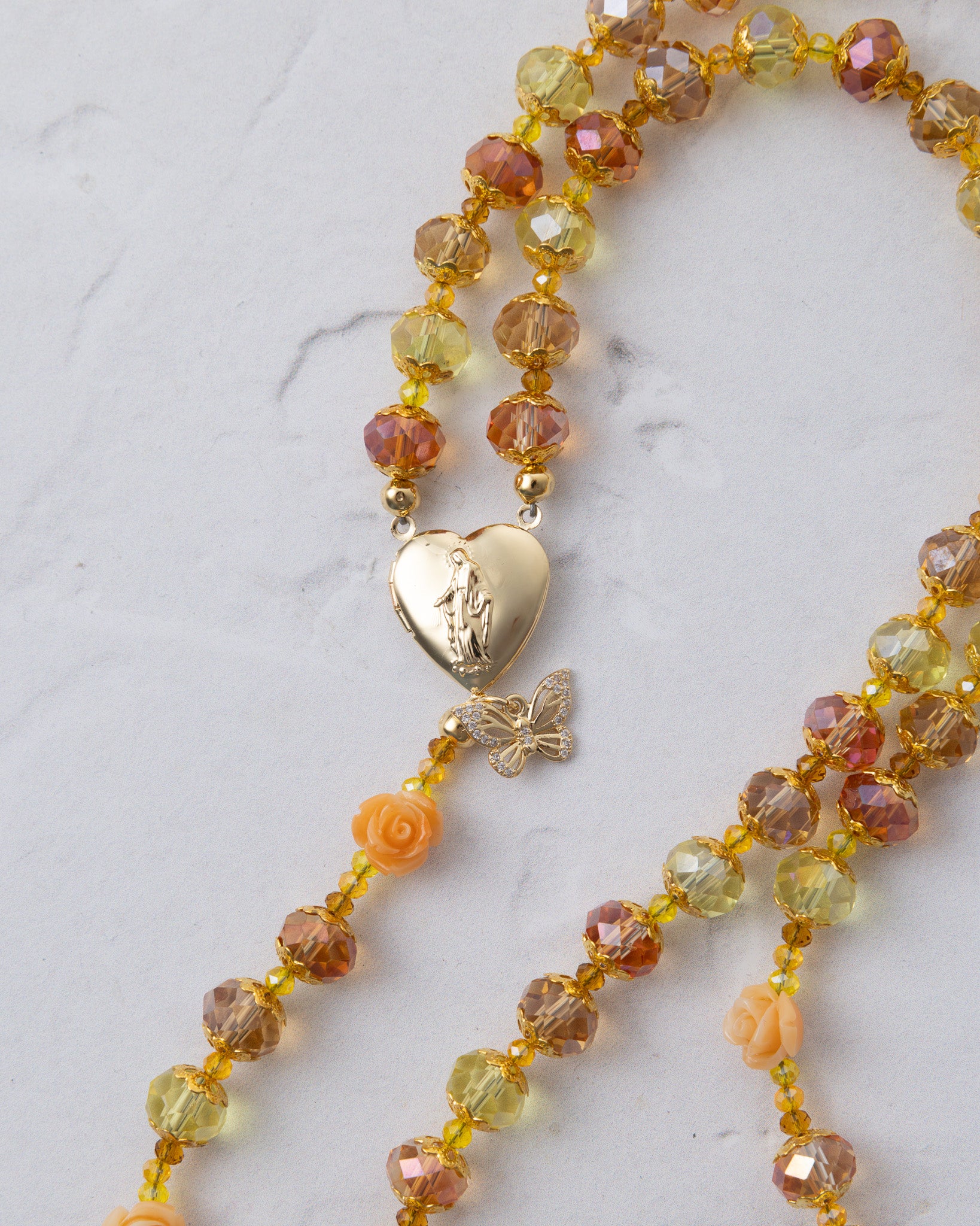 A delicate gold-toned metamorphosis rosary with faceted amber yellow beads and a heart-shaped locket pendant with butterfly charm