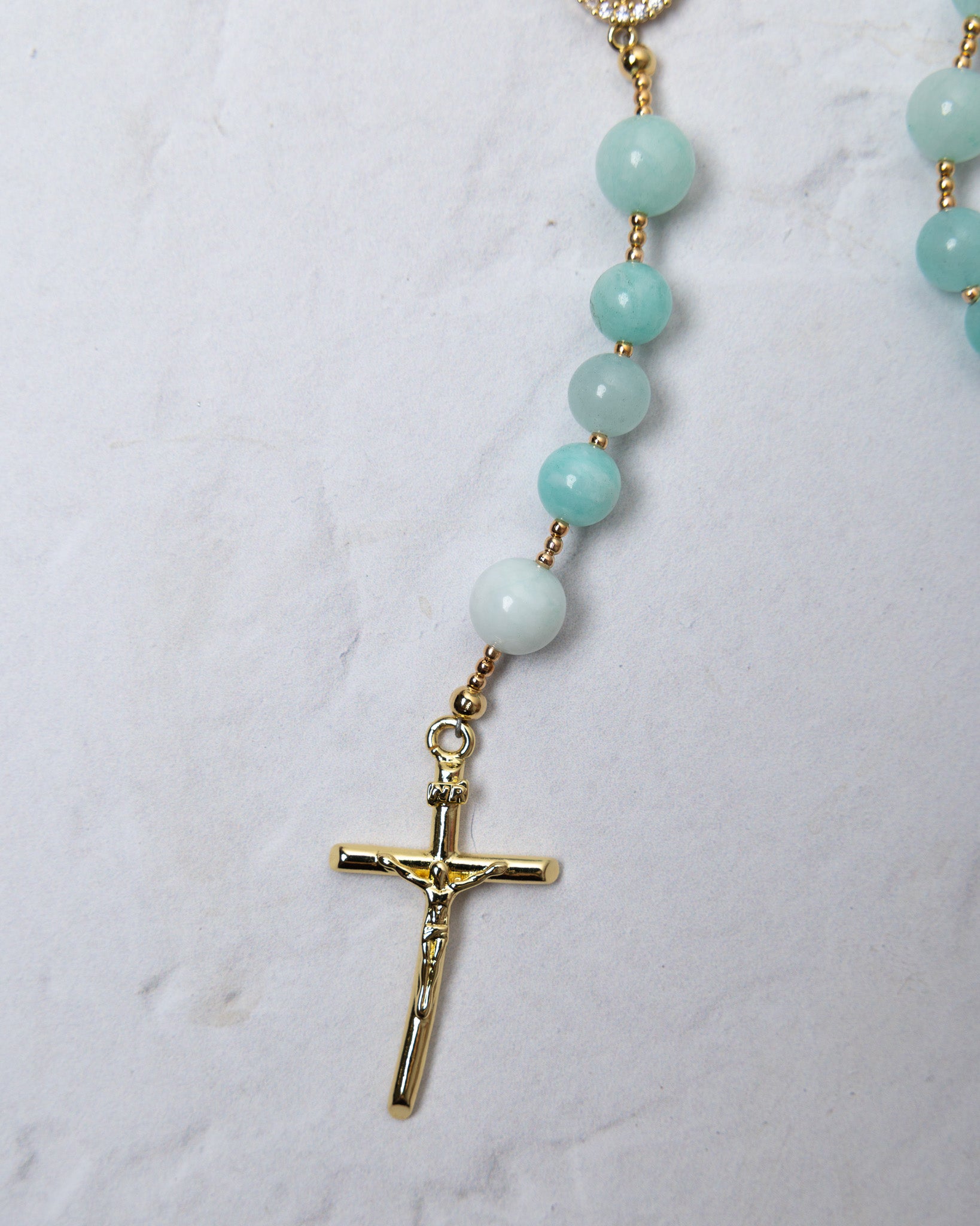 A delicate hydrangea rosary with light blue jade beads and a gold toned crucifix for prayer and devotion