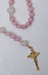 A sweet pea rosary with soft pink and translucent rose quartz beads and a gold-toned crucifix pendant