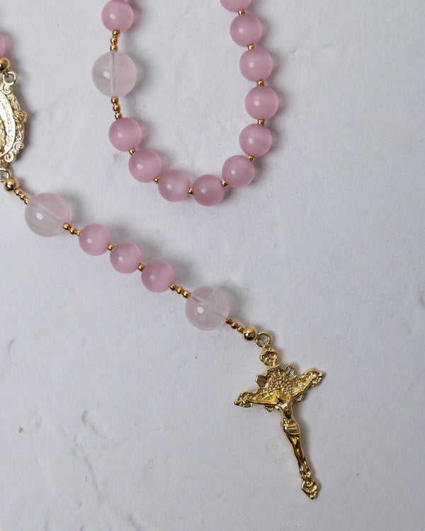 A sweet pea rosary with soft pink and translucent rose quartz beads and a gold-toned crucifix pendant