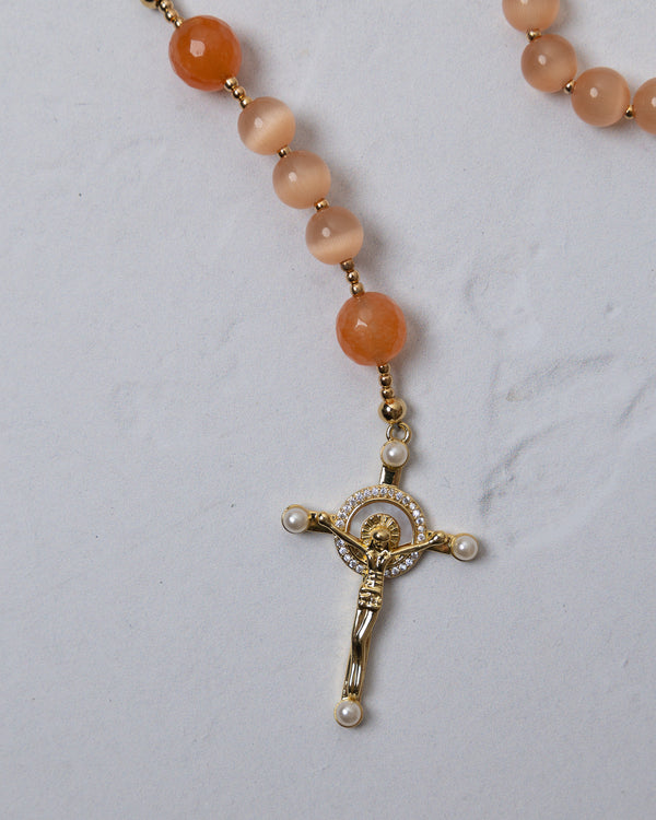 A gold-toned crucifix pendant with clear crystals and pearl accents on an orange carnelian bead poppy rosary