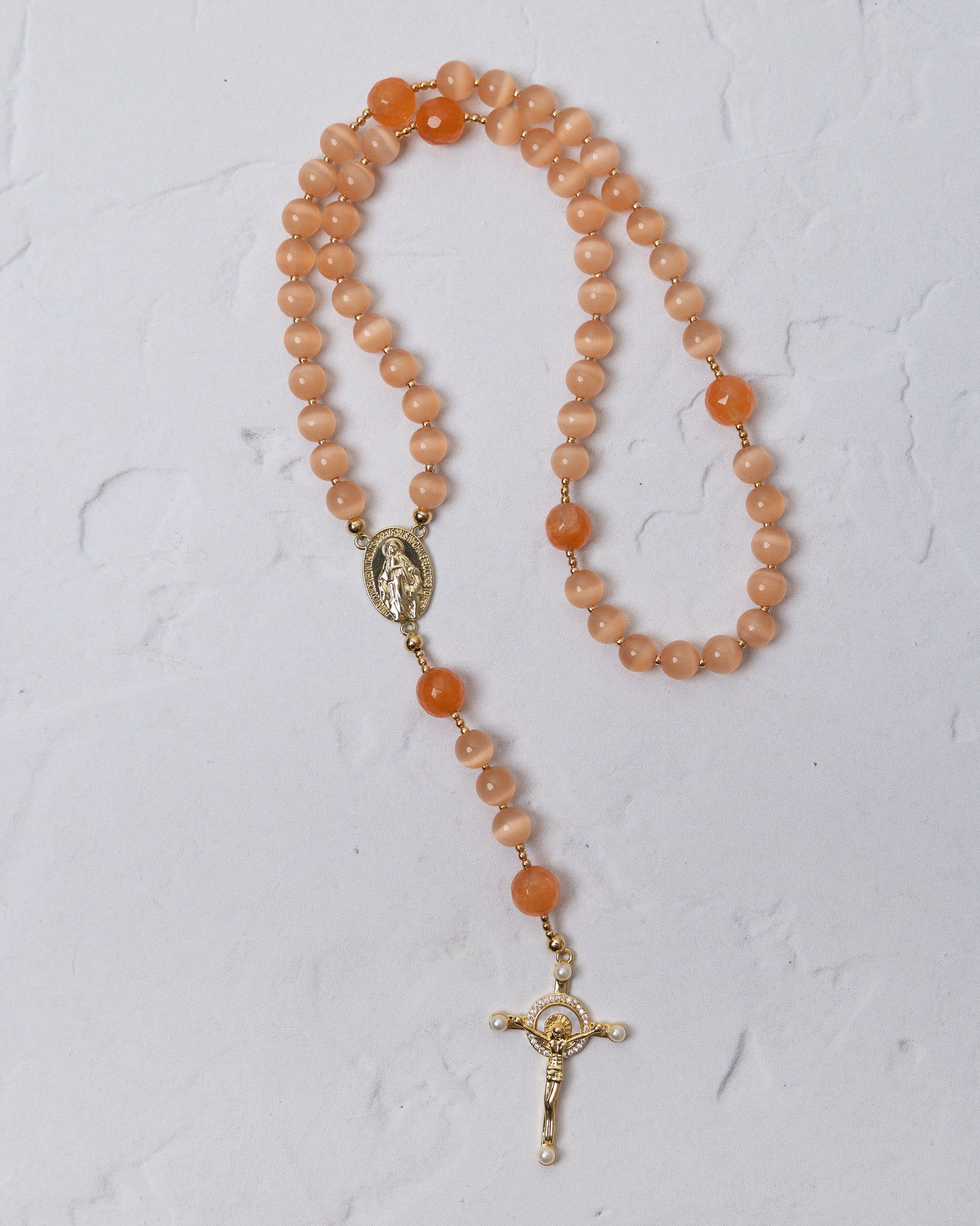 A peach-colored carnelian poppy rosary with gold-toned metal accents and a crucifix for prayer and meditation