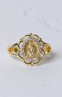 Gold-toned marian halo ring featuring an ornate floral design with a central religious figure and clear stones