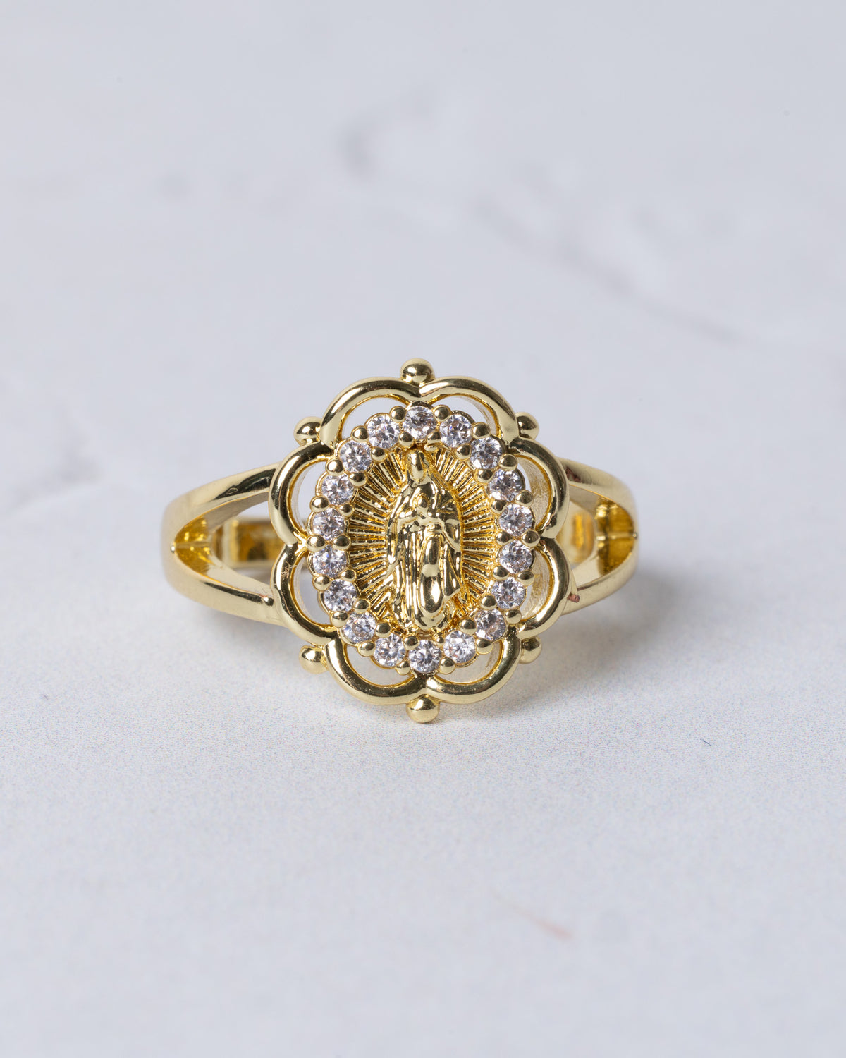 Gold-toned marian halo ring featuring an ornate floral design with a central religious figure and clear stones