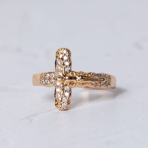Gold-toned crucifix ring with clear sparkling stones along the cross arms and detailed figure at the center