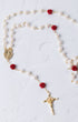 A delicate rosary featuring white pearls, red rose accents, and gold-toned metal components including a crucifix and an oval medallion.