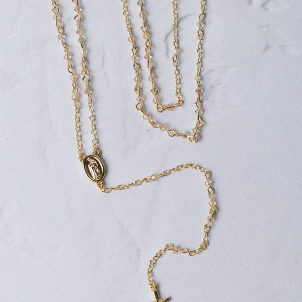The forever rosary necklace is a gold-toned rosary necklace with a delicate chain and a small oval medallion