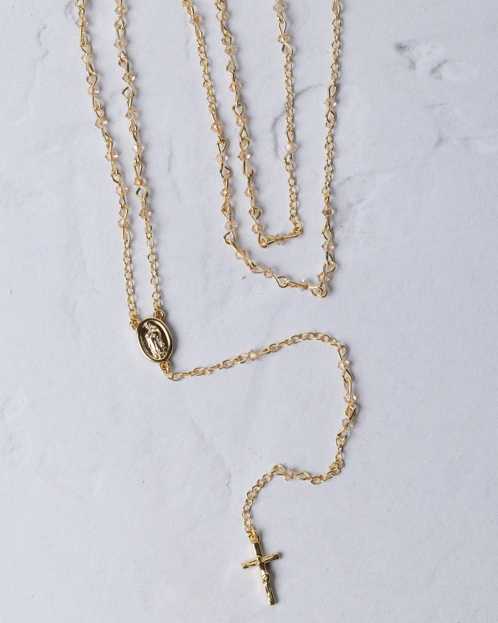 The forever rosary necklace is a gold-toned rosary necklace with a delicate chain and a small oval medallion