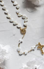 pearl heart shaped rosary with delicate gold accents and cross details on a light marble surface
