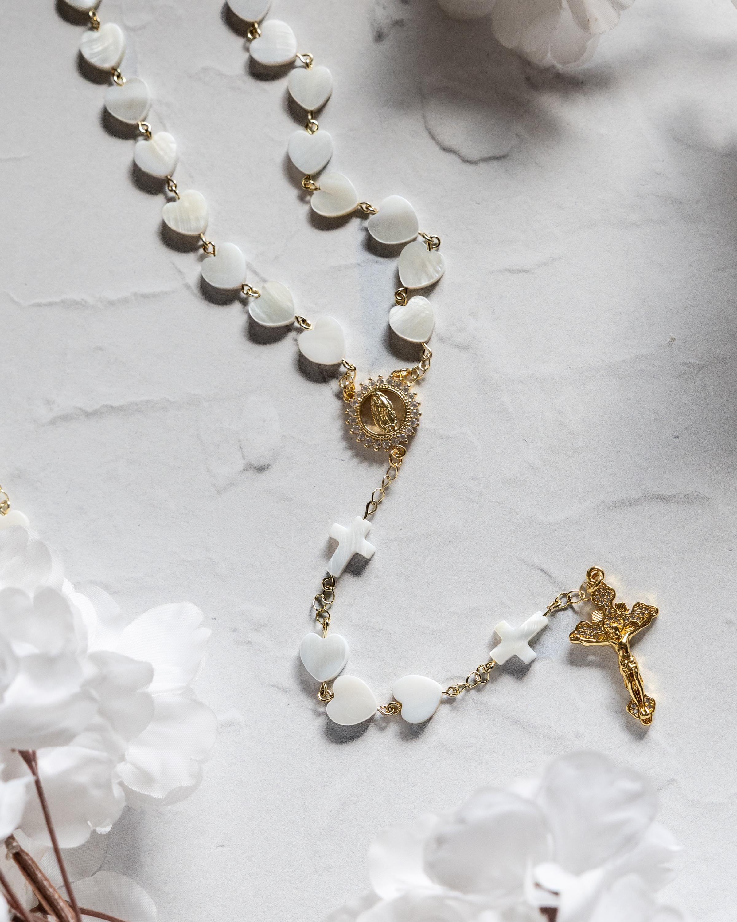 pearl heart shaped rosary with delicate gold accents and cross details on a light marble surface