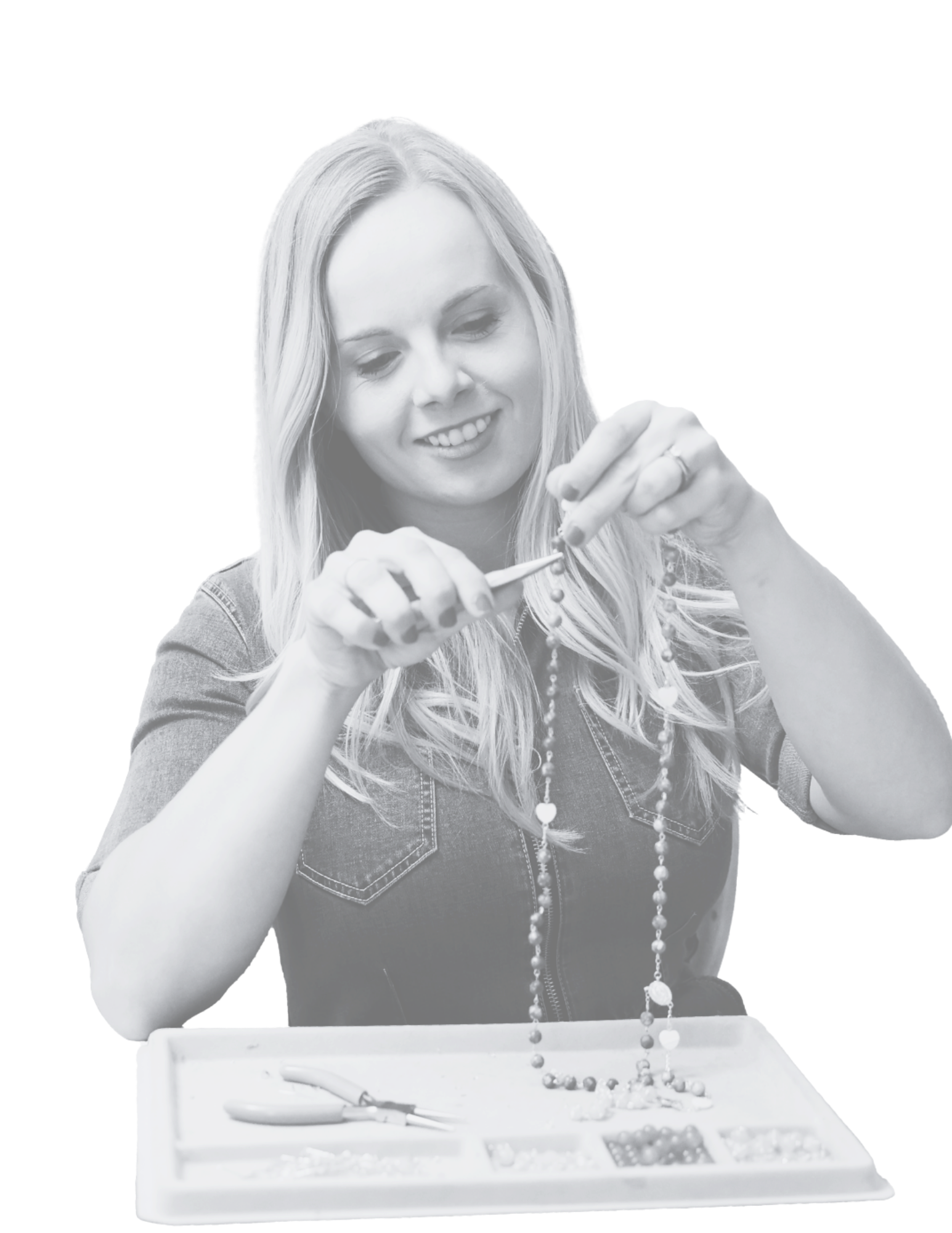 A woman wearing a denim shirt is holding and adjusting a beaded necklace with heart-shaped charms.