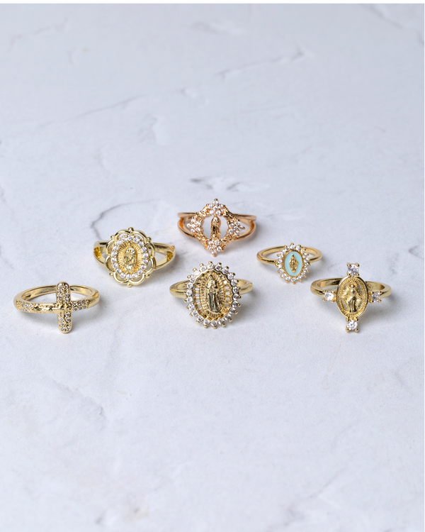 A set of seven gold-toned religious rings, each featuring intricate designs with embedded crystals and depictions of the virgin mary or a cross.