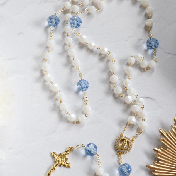 Elegant rosary with white and blue beads, gold chain, featuring a golden crucifix and medallion.
