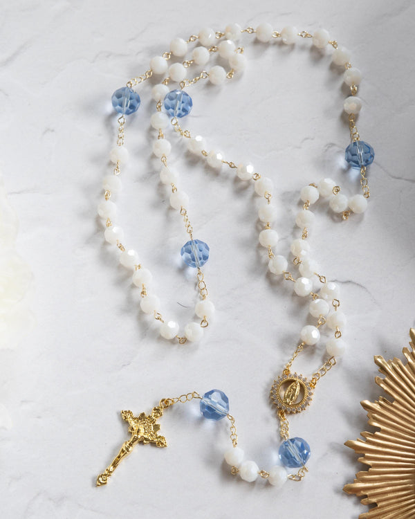 Elegant rosary with white and blue beads, gold chain, featuring a golden crucifix and medallion.