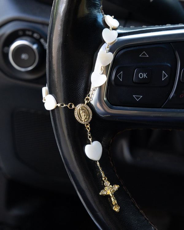 White heart rosary with gold accents on car steering wheel